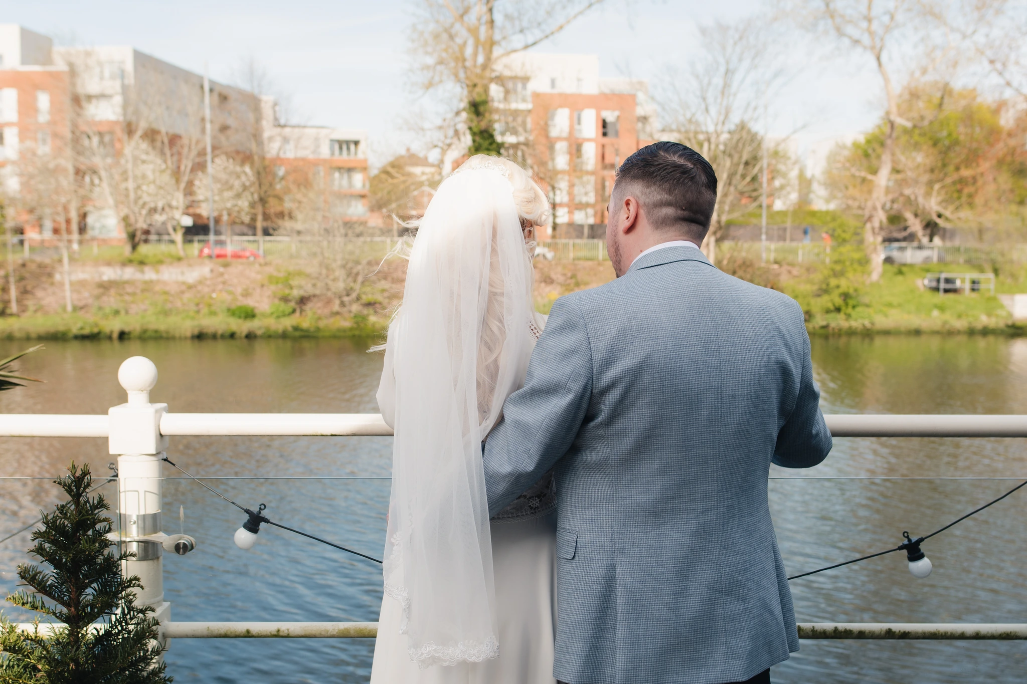 a bride and groom stand on a balcony overlooking a river