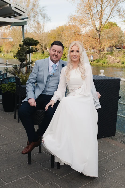 a bride and groom sitting on a bench in front of a river