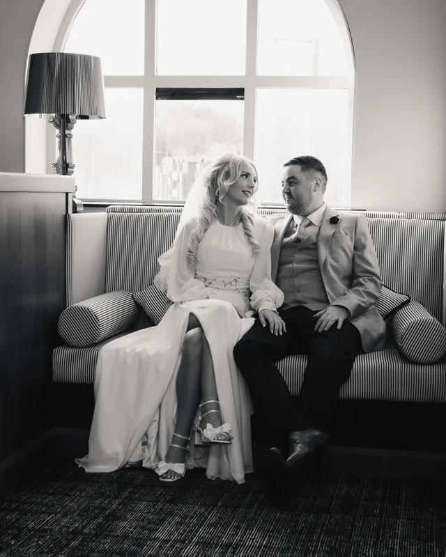 a bride and groom sit on a sofa in a hotel room