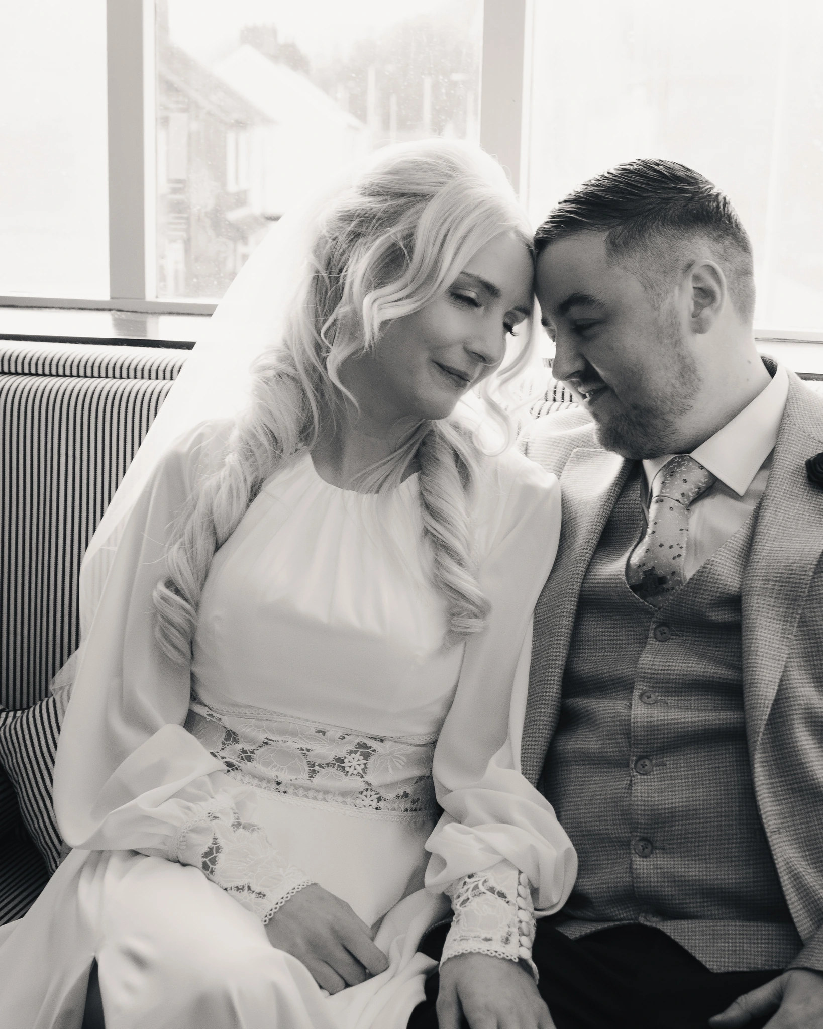 a bride and groom are sitting on a sofa in front of a window