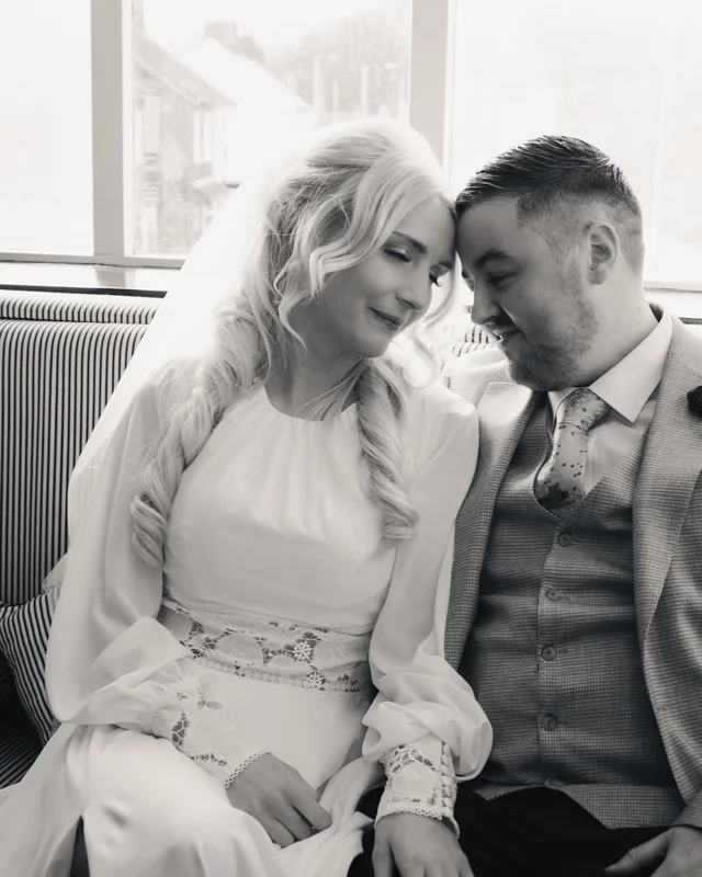 a bride and groom are sitting on a sofa in front of a window
