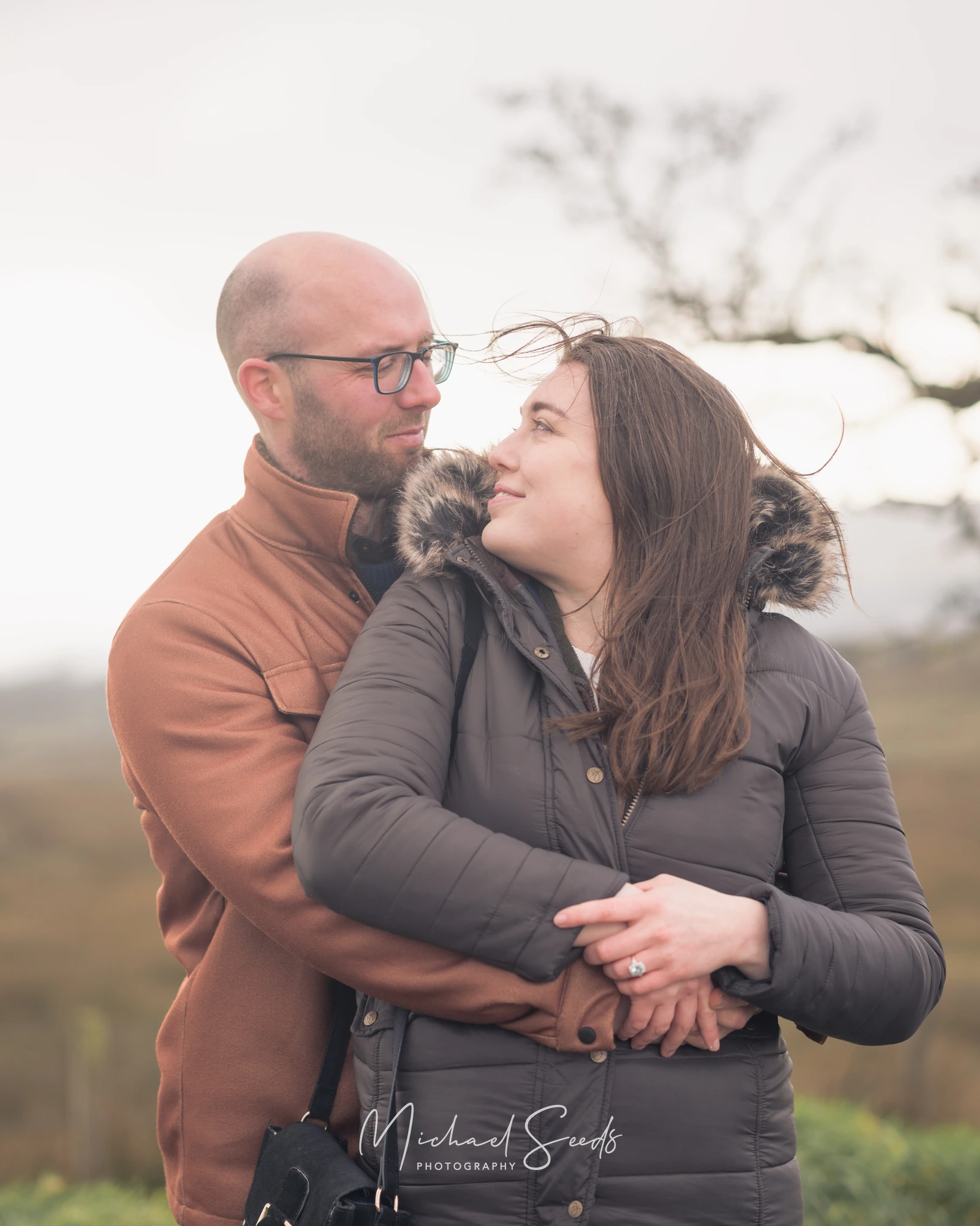 a couple hugging in front of a tree in a field