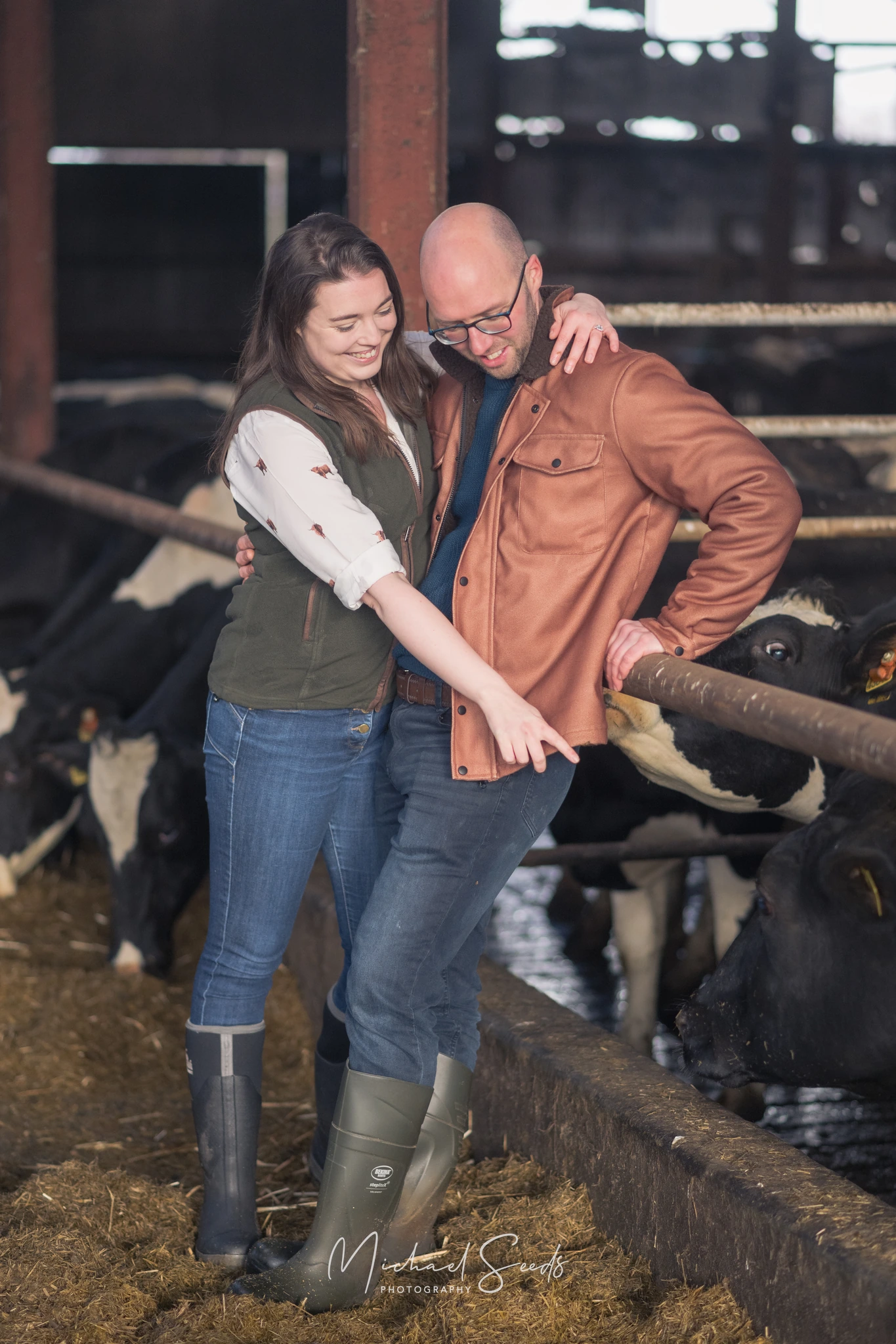 a man and woman standing in front of a barn with cows in the background