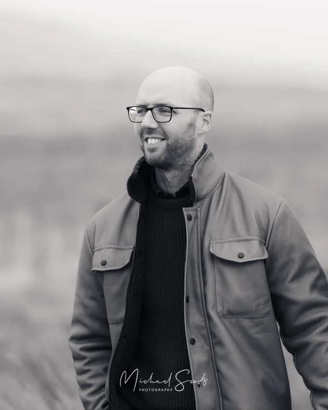 a man with glasses smiles in a field
