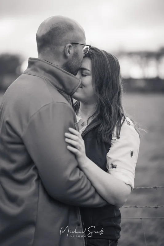 a couple kissing in a field with a fence in the background