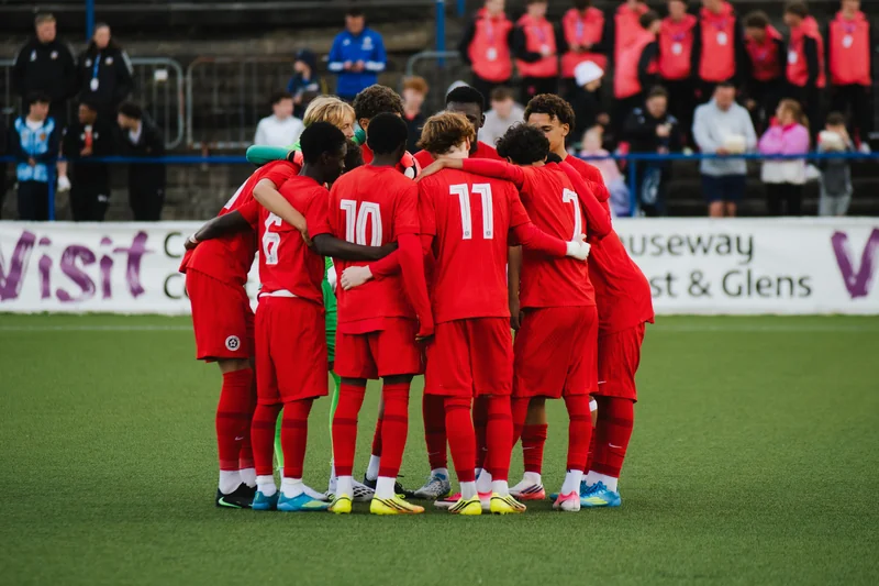 a group of soccer players huddle in a circle on a pitch
