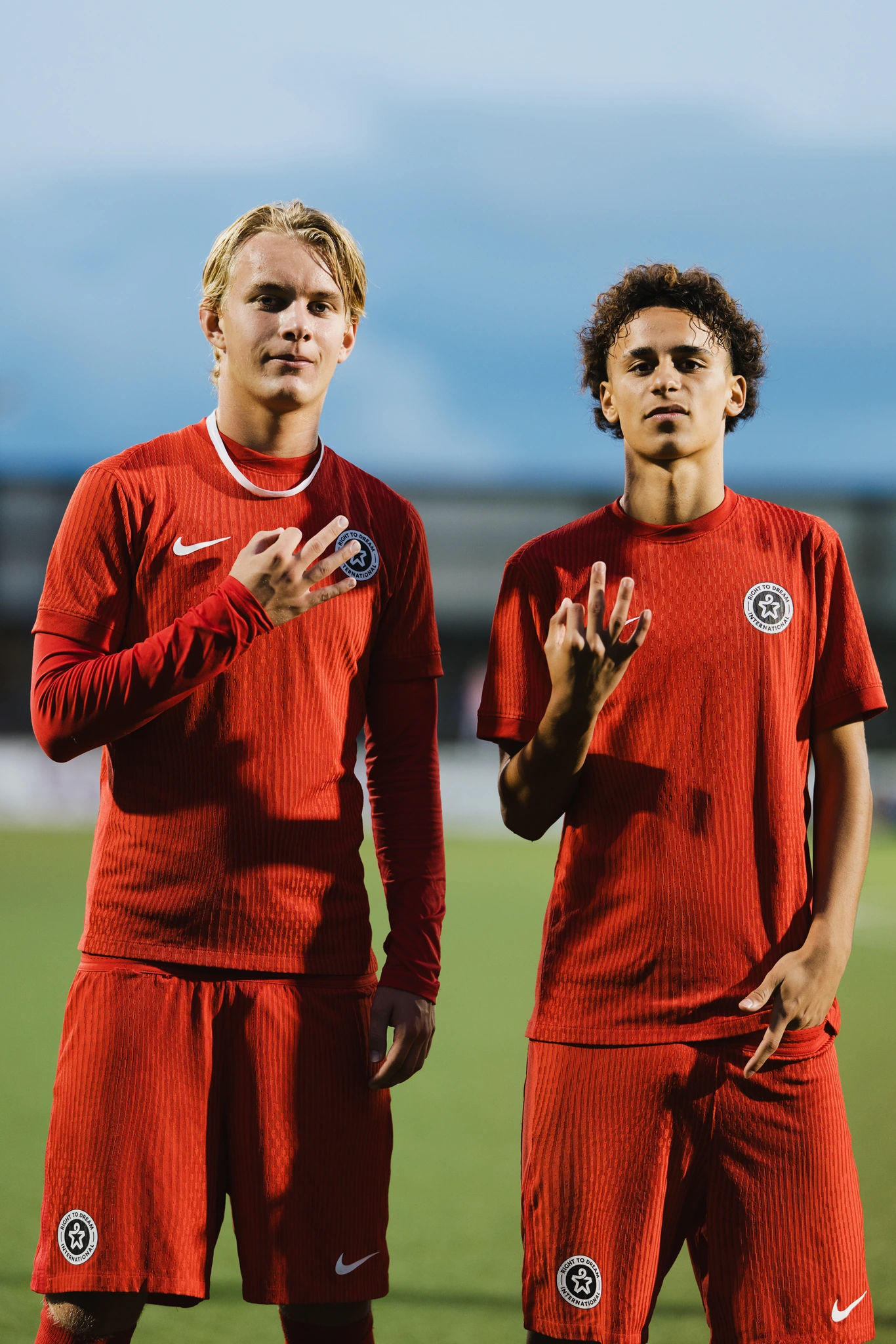 two young men in red soccer uniforms posing for the camera on a soccer field