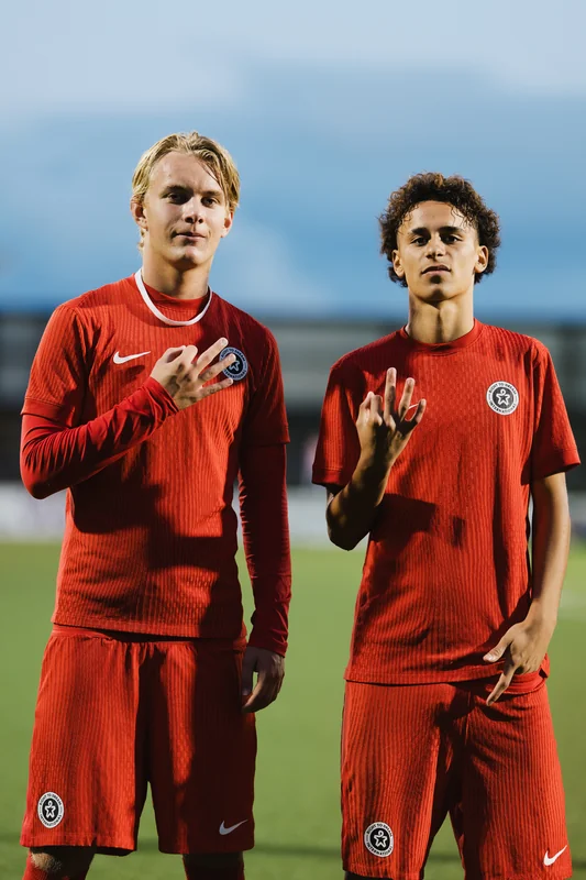 two young men in red soccer uniforms posing for the camera on a soccer field