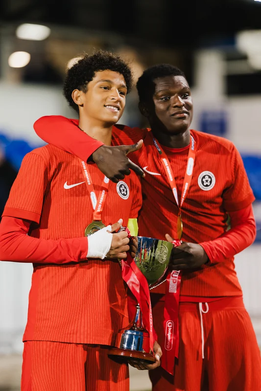 two men in red soccer uniforms posing with their trophies