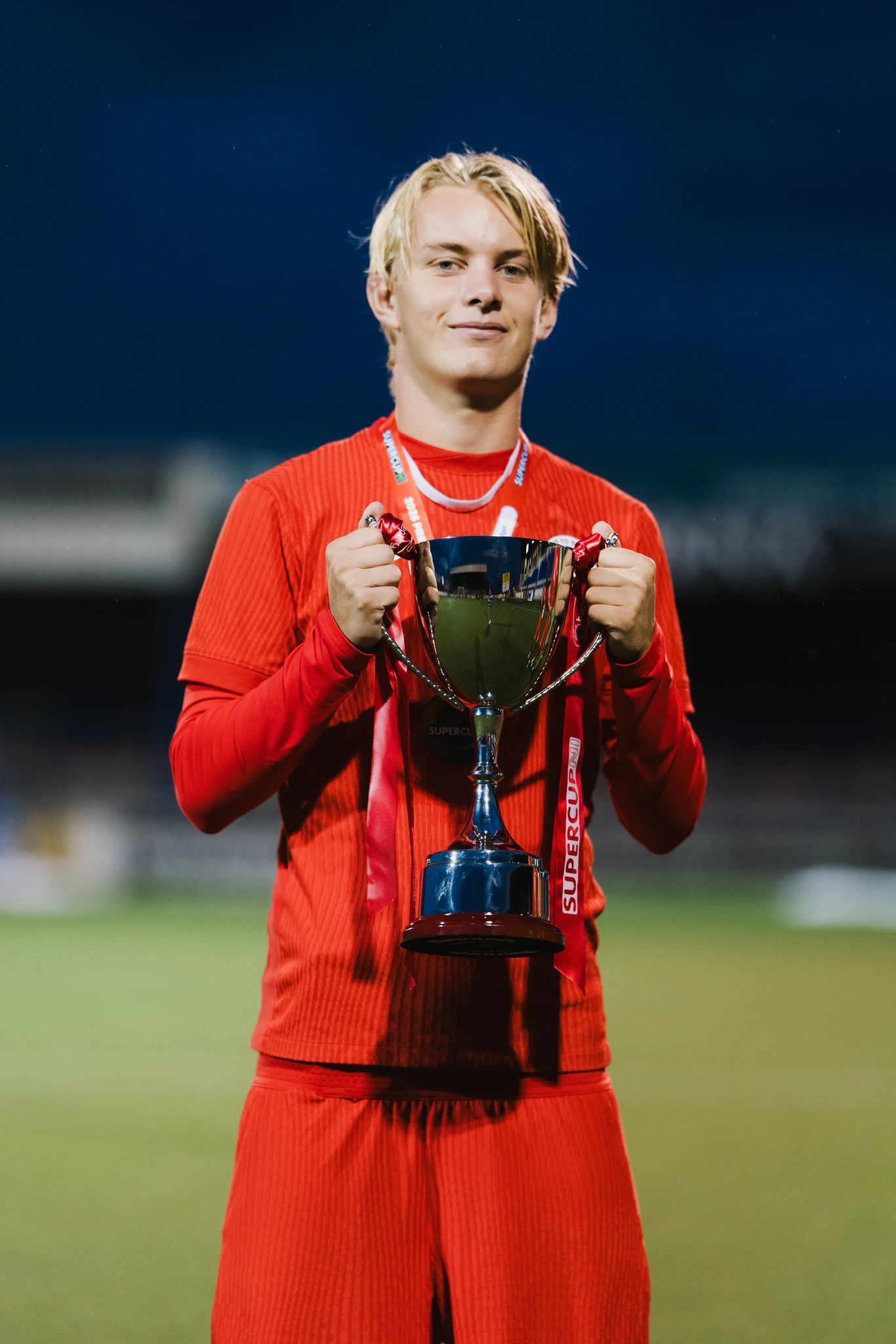 a young man holding a trophy in front of a soccer field