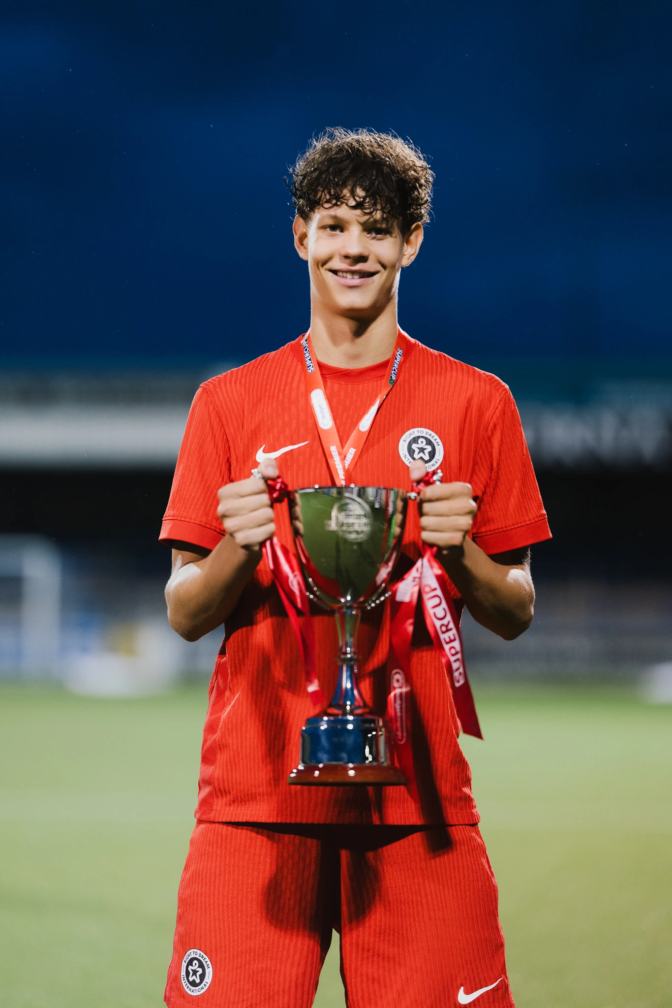 a young man holding a trophy in front of a soccer field