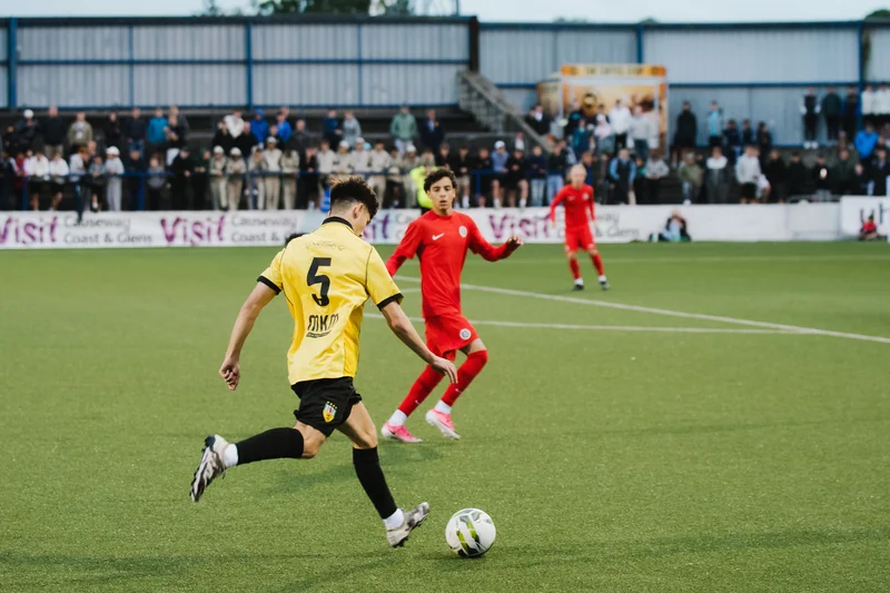 a man in a red shirt kicks a ball in front of a crowd