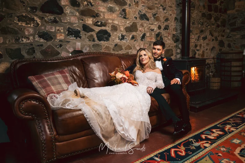 a bride and groom sitting on a sofa in front of a fireplace