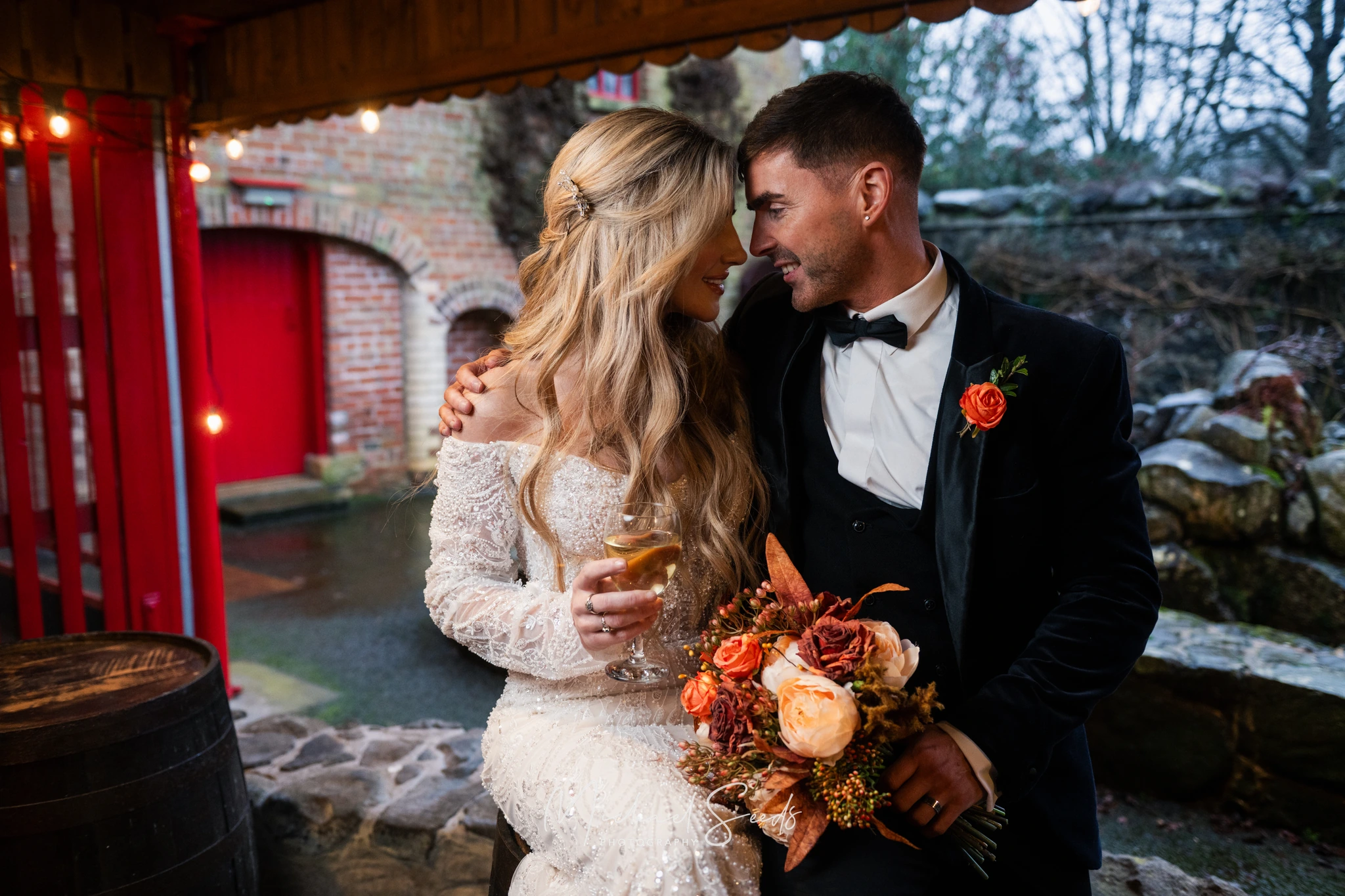 a bride and groom kissing in front of a red wine barrel