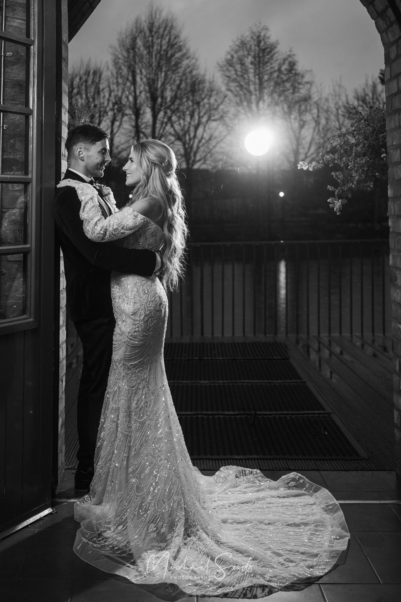 a bride and groom kiss in front of a window at dusk