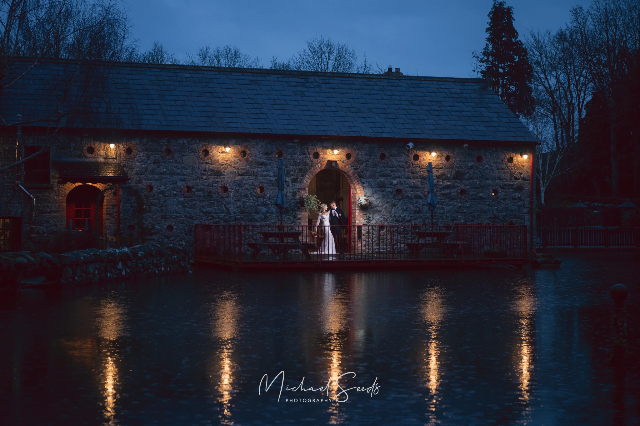 a bride and groom standing in front of a barn at dusk