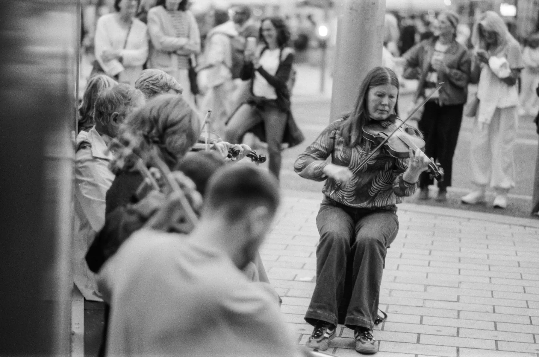 A fiddle player performing as a crowd gathers behind her.