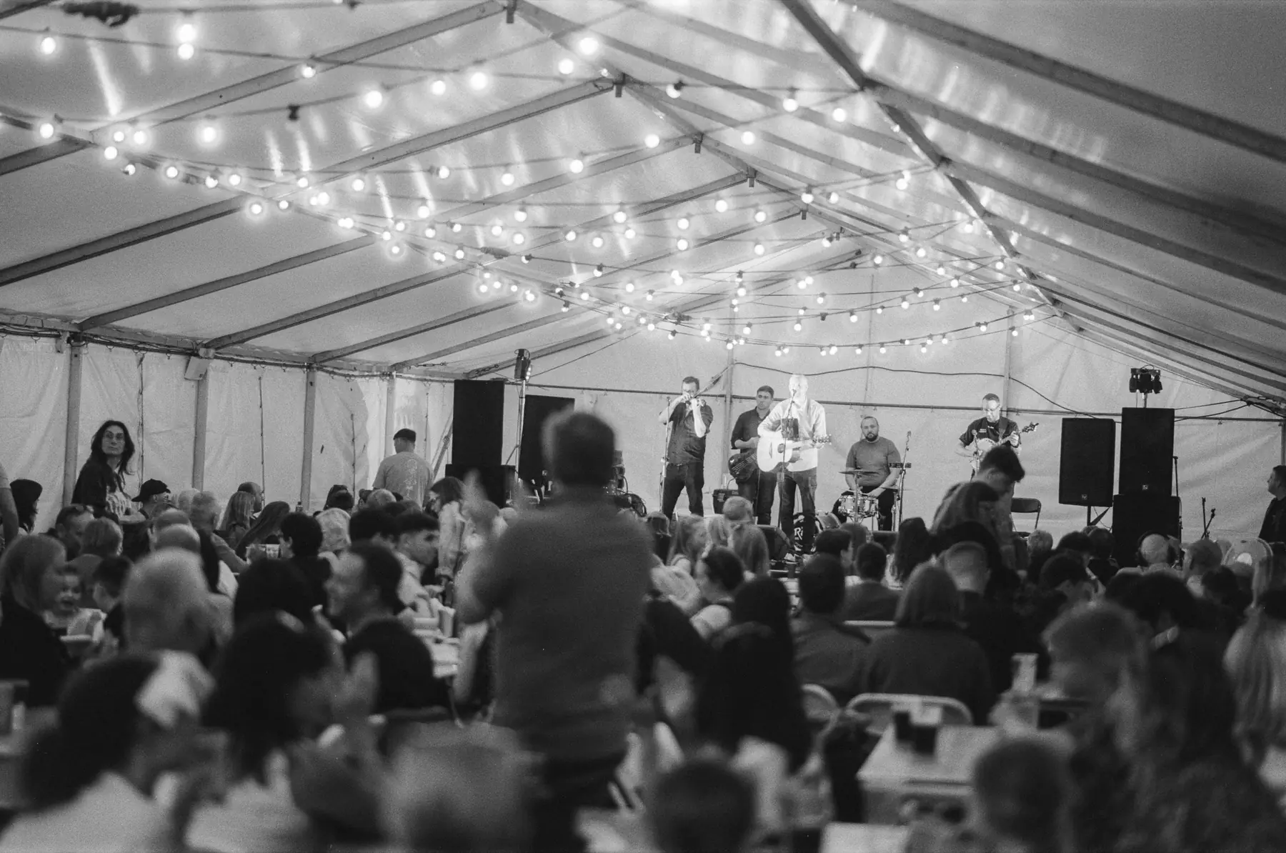 A crowded performance tent lit by strings of lights.