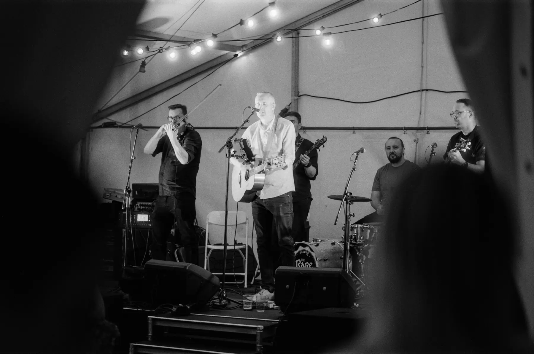 Musicians performing on stage framed by people in the foreground.