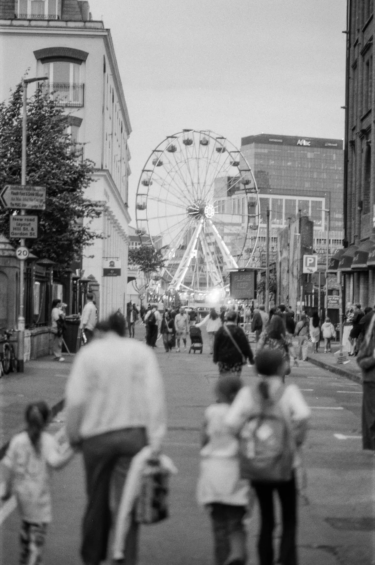 People moving through Belfast with a Ferris wheel visible down the street.