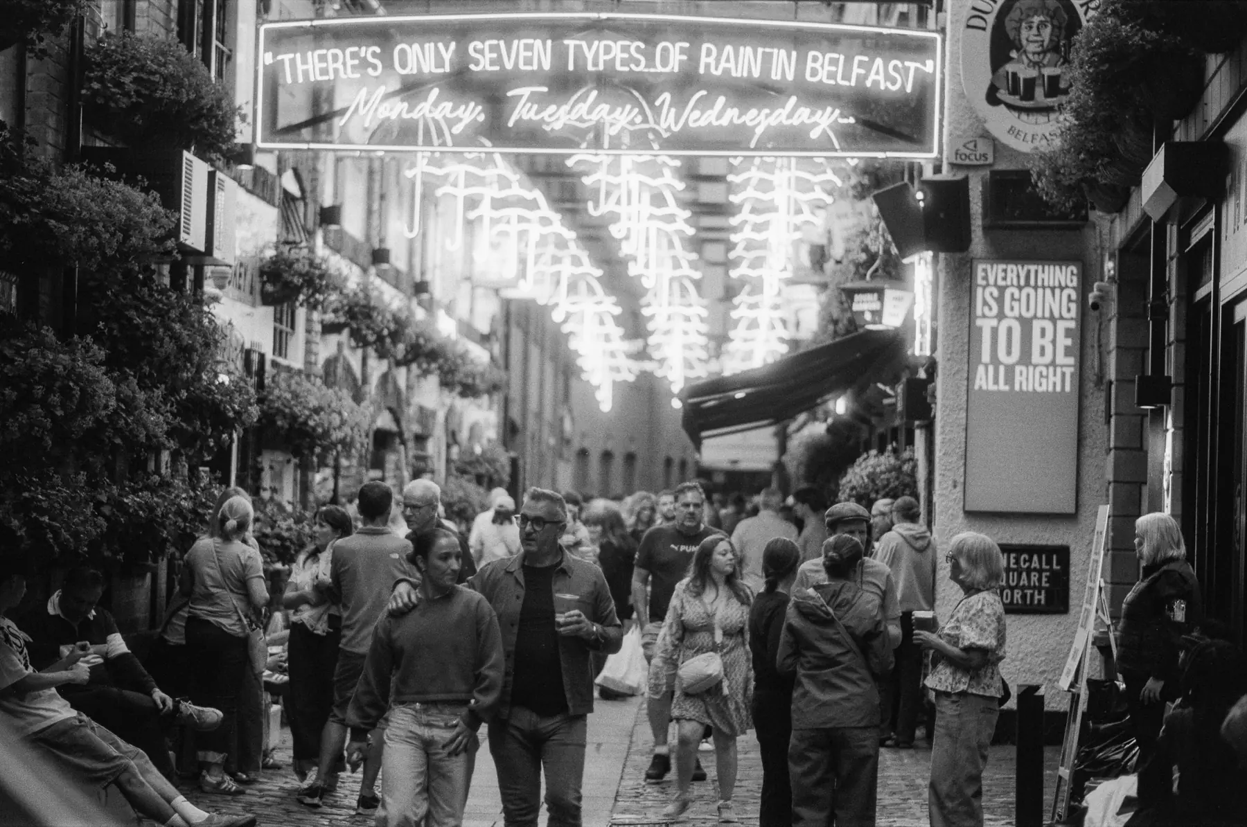 A busy Belfast street beneath illuminated signs about the city's rain.